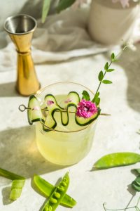 green cocktail with purple flower and pea shot garnish