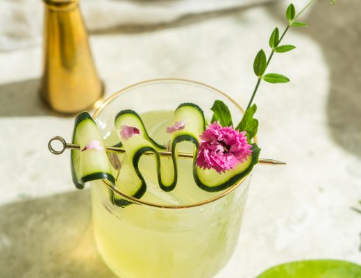 green cocktail with purple flower and pea shot garnish